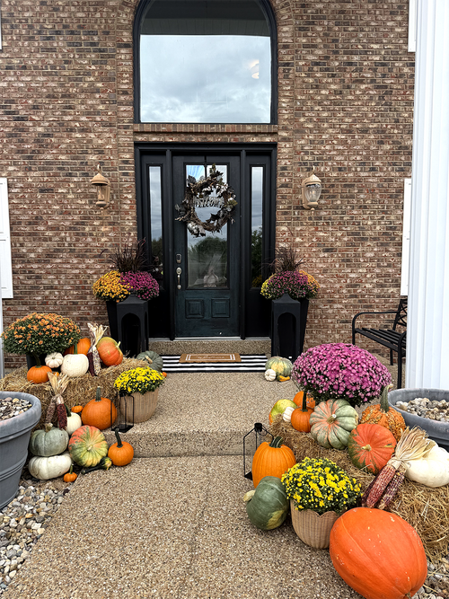 Fall pumpkins, mums and straw bales arranged at a brick home entrance
