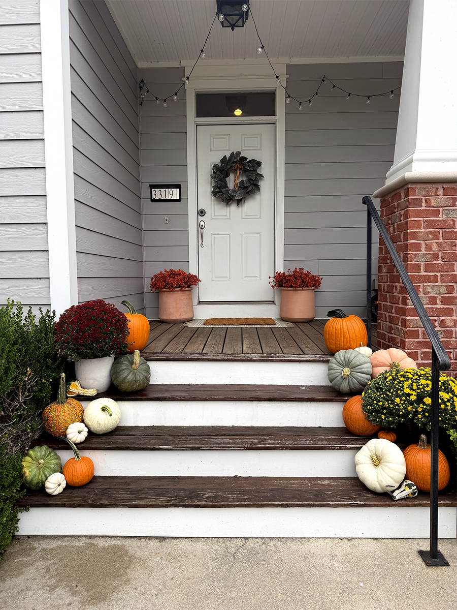 Pumpkins and mums decorating the steps of a covered autumn porch